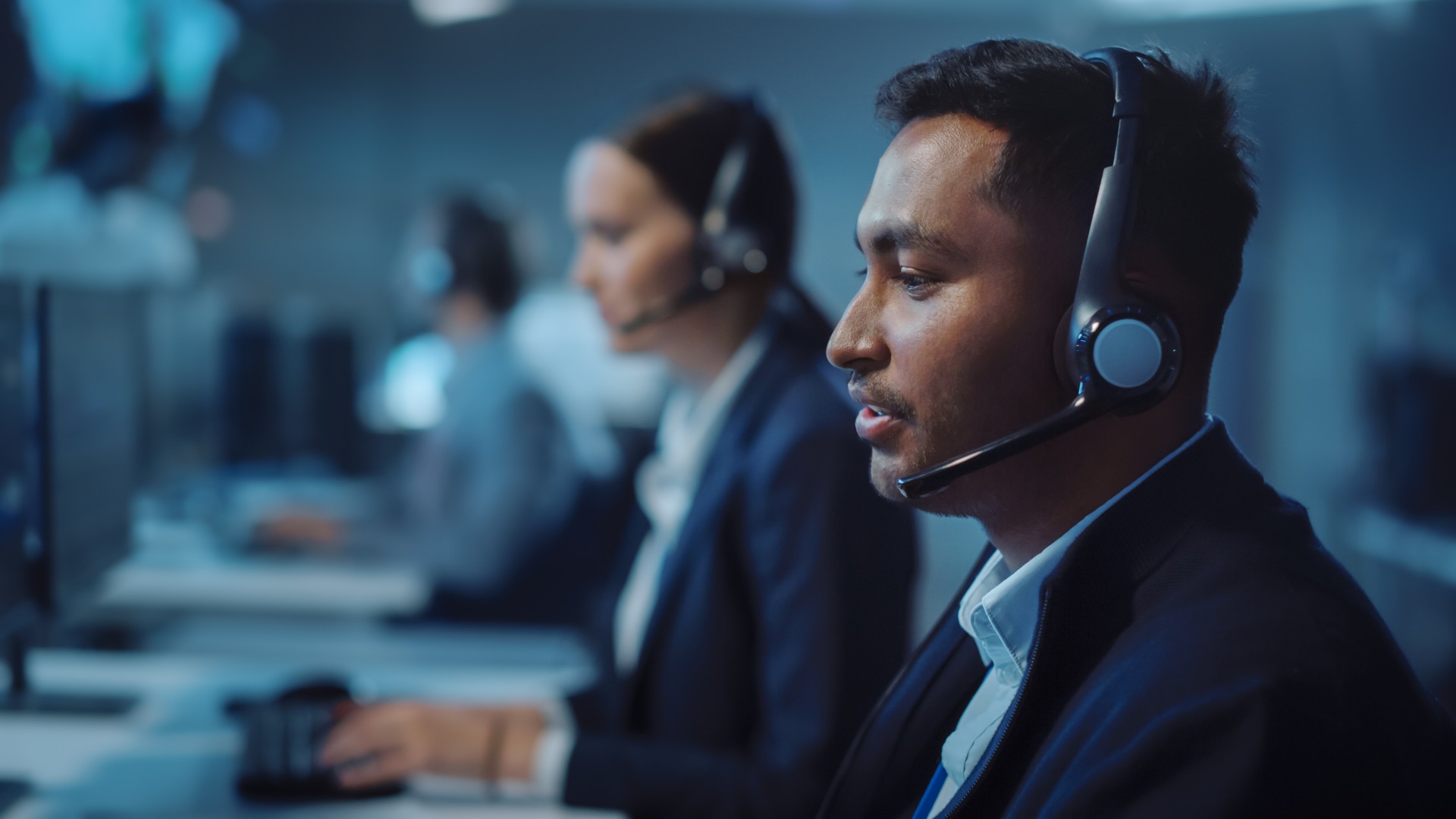 Close Up Portrait of a Joyful Technical Customer Support Specialist Talking on a Headset while Working on a Computer in a Call Center Control Room Filled with Computer Display Screens and Data Servers